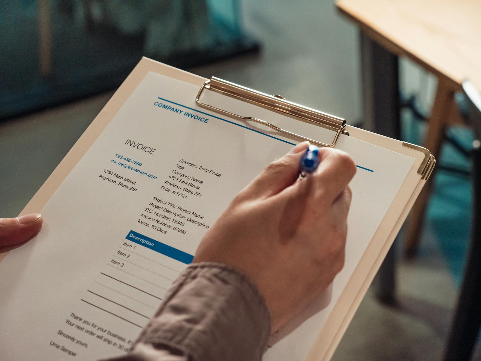 Hand filling out a Company Invoice form on a clipboard with a pen