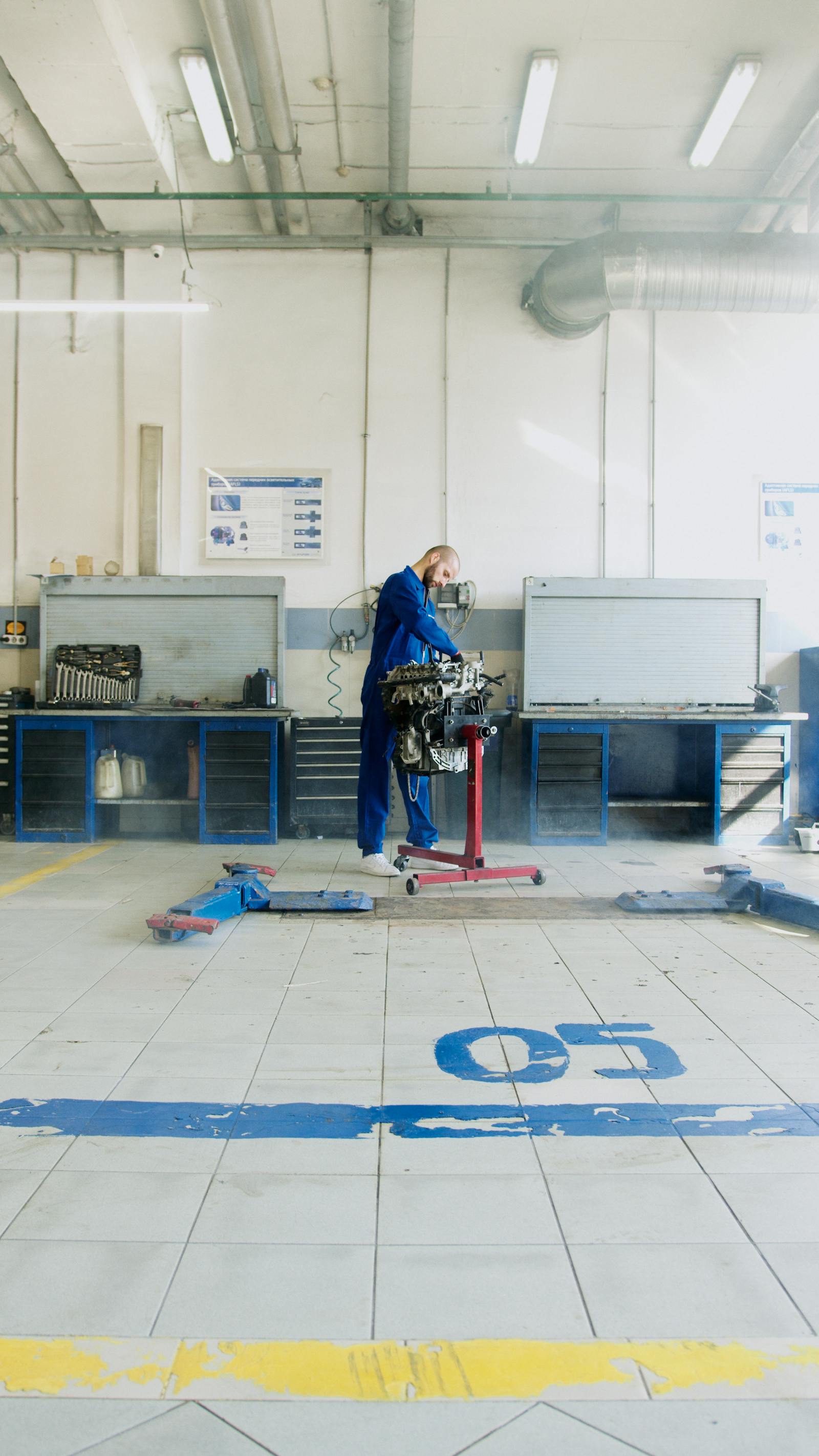 Mechanic in blue overalls leaning over an engine bay