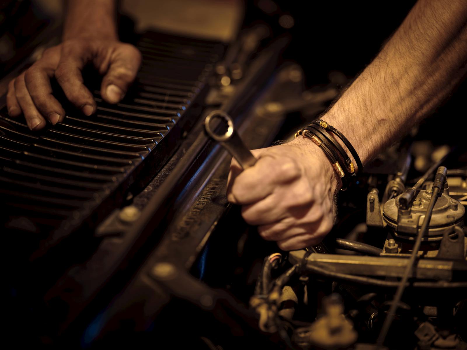 Weathered mechanic hands tightening a bolt on an engine with a wrench