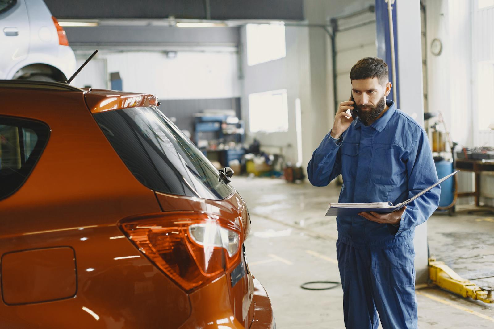 Mechanic on a smartphone call next to a red car under repair