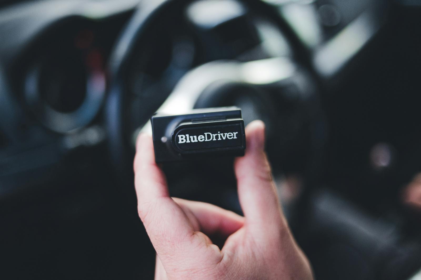 Hand holding an OBD2 scanner near a vehicle dashboard