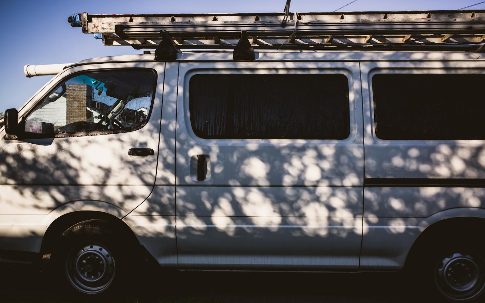 White service van with extension ladder casting strong shadow on a sunlit wall